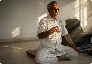 Yoga teacher in white attire speaking while seated beside a stone shrine during a philosophy session